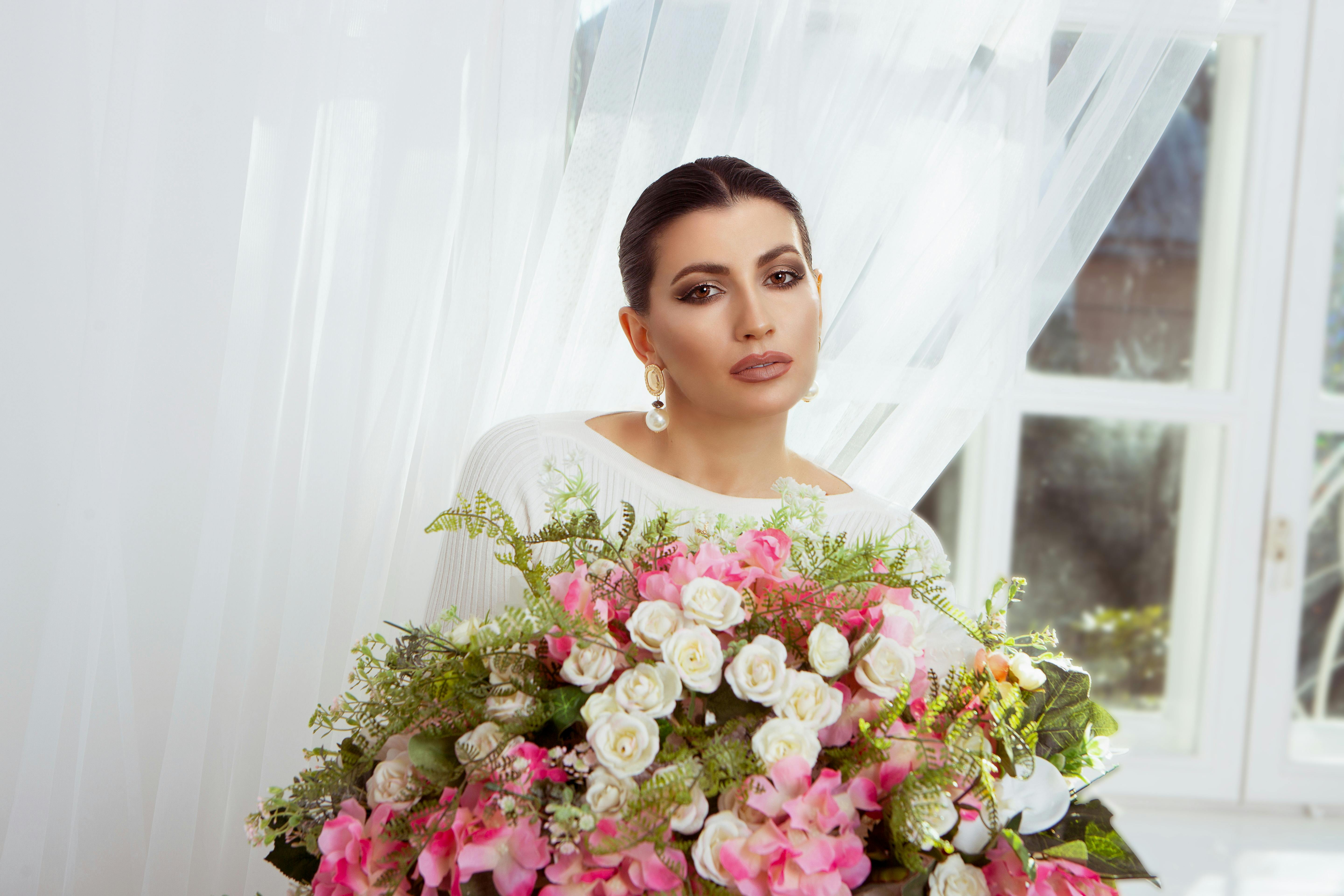 Beautiful woman with a bouquet of pink and white flowers indoors, exuding elegance and charm.